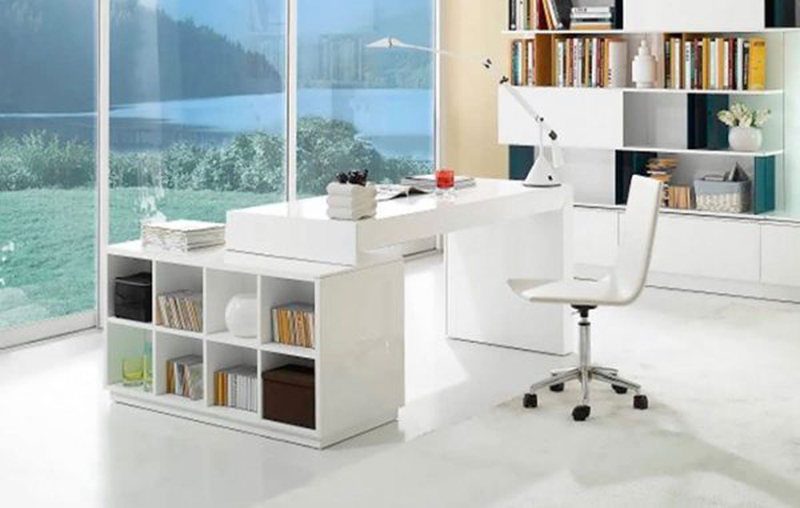 Kệ đựng sách và bàn làm việc màu trắng gắn liền nhau được đặt trong không gian làm việc thoáng mát, phía trước là cửa kính hướng ra ngoài có cảnh vật thiên nhiên
