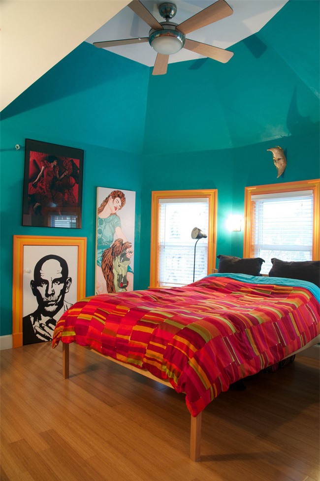 Một phòng ngủ màu ngọc lam được tạo điểm nhấn với bộ đồ giường màu đỏ và khung cửa sổ màu vàng sáng