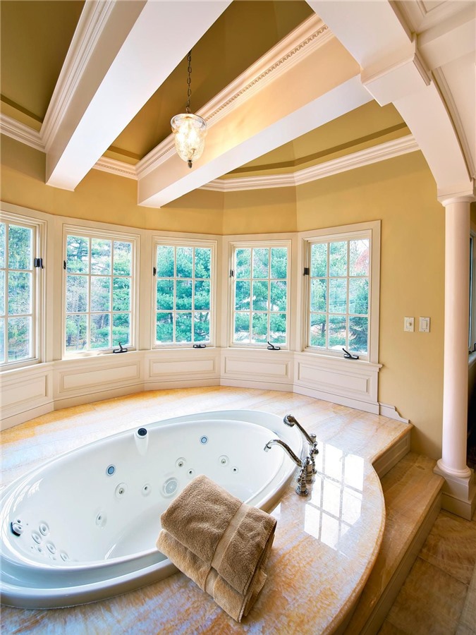 Phòng tắm lớn có rất nhiều cửa sổ và dầm trên trần nhà, với một bồn tắm hình bầu dục lớn cộng với một sàn đá xung quanh