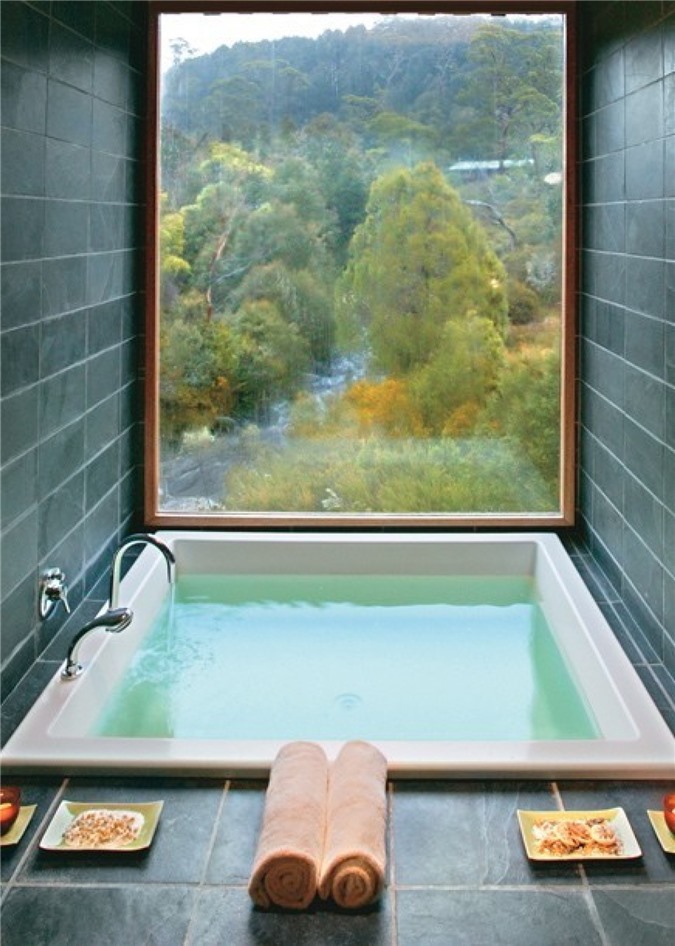Phòng tắm lát gạch màu xám với cửa sổ toàn cảnh để ngắm cảnh và bồn tắm chìm để thư giãn hết mức có thể
