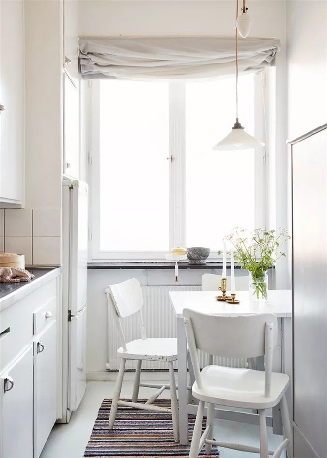 Nhà bếp nhỏ với các tủ màu trắng sáng và đèn mặt dây chuyền không đối xứng, theo đó là sự pha trộn thú vị của đồ nội thất theo phong cách đồng quê retro và rèm cửa vải lanh.