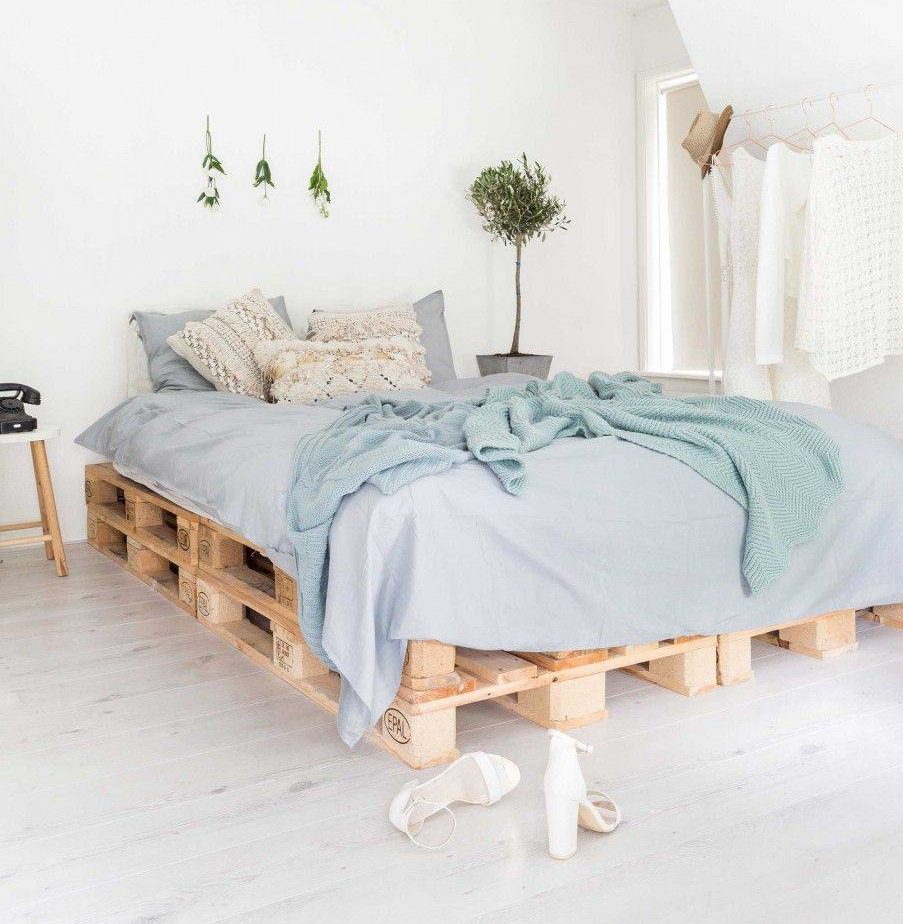 Một phòng ngủ sang trọng ven biển, sạch sẽ dựa trên nền tảng pallet gỗ mộc mạc làm khung giường và sử dụng bộ khăn trải giường bằng vải lanh màu xanh nhạt để hoàn thiện vẻ ngoài
