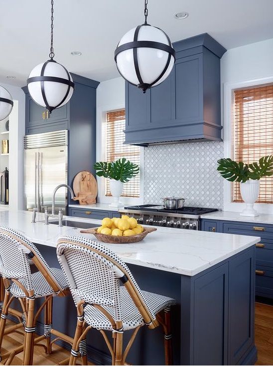 hà bếp nhiệt đới mát mẻ với tủ màu xanh lam và một chiếc bếp phù hợp, tấm lát nền bằng gạch, mặt bàn bằng đá trắng và những chiếc ghế đẩu bắt mắt