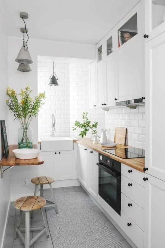 căn bếp nhỏ màu trắng ấm cúng với máy hút mùi kết hợp, mặt bếp bằng butcherblock và các thiết bị tích hợp cùng với khu vực ăn uống nhỏ