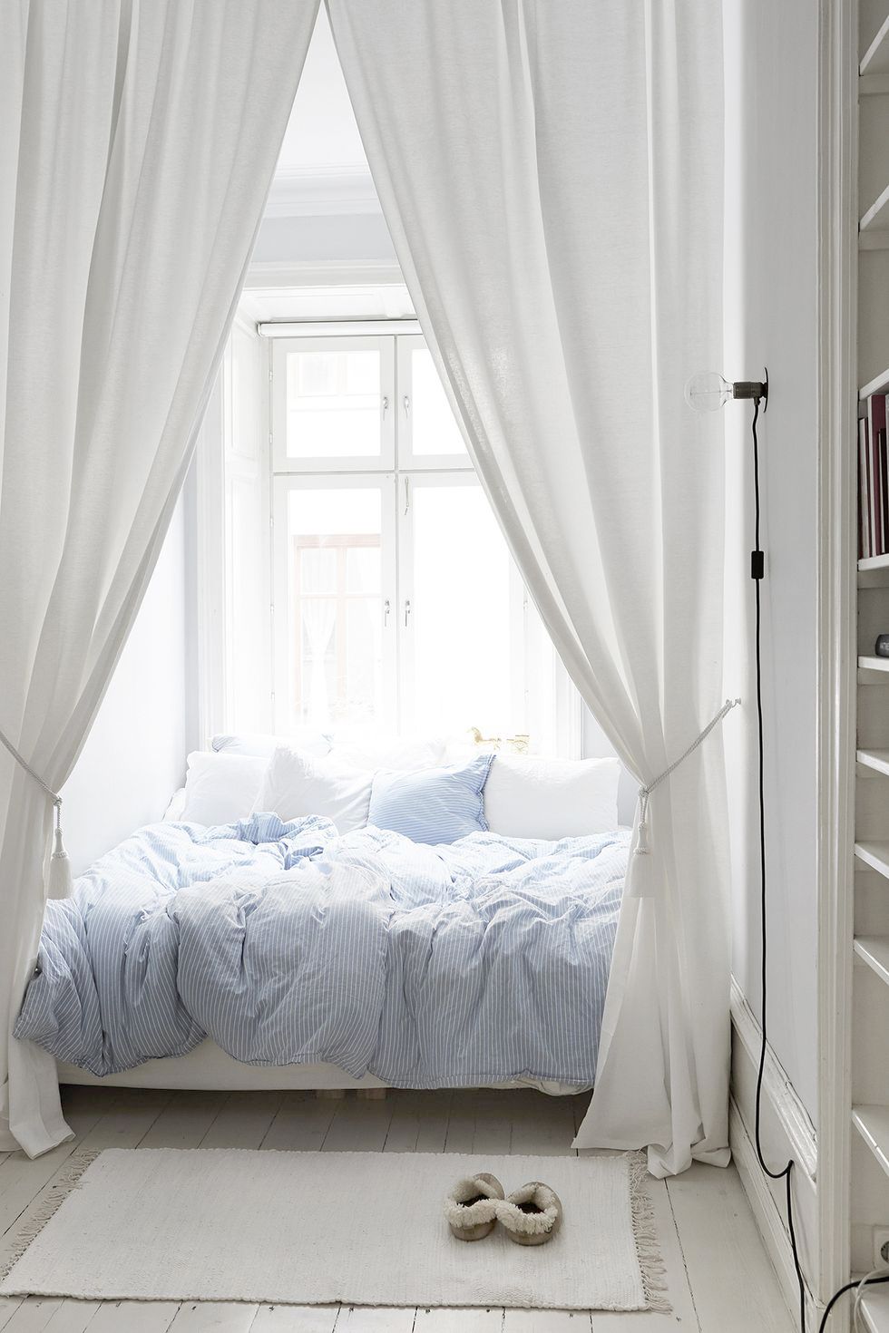 Treo rèm cửa cao đến trần quanh giường sẽ trông ấn tượng và mơ mộng hơn so với một chiếc rèm cửa cổ điển và bộ chăn ga gối đệm màu xanh nhạt trong phòng ngủ này làm tăng thêm nét vui tươi.
