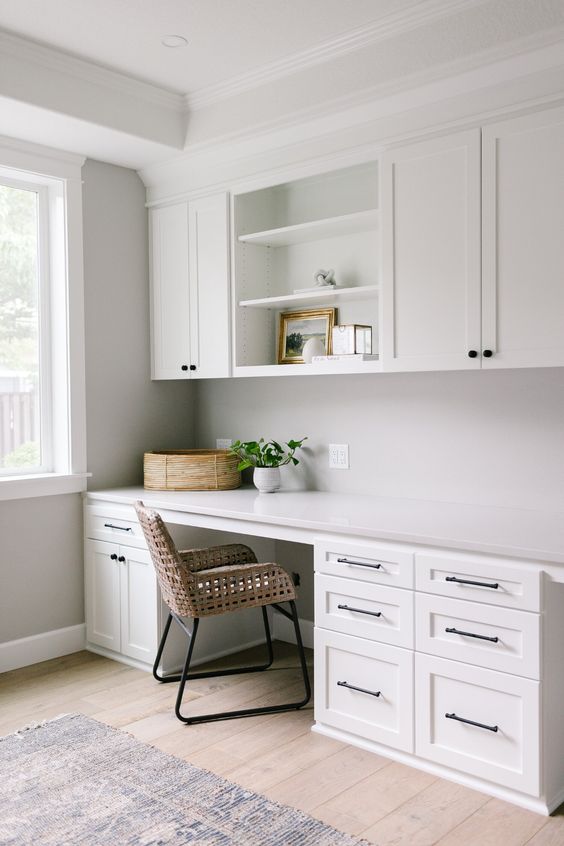 Không gian với phong cách trung tính hiện đại tại nhà với tủ kiểu shaker màu trắng, bàn làm việc có nhiều đồ, ghế mây và một số cây