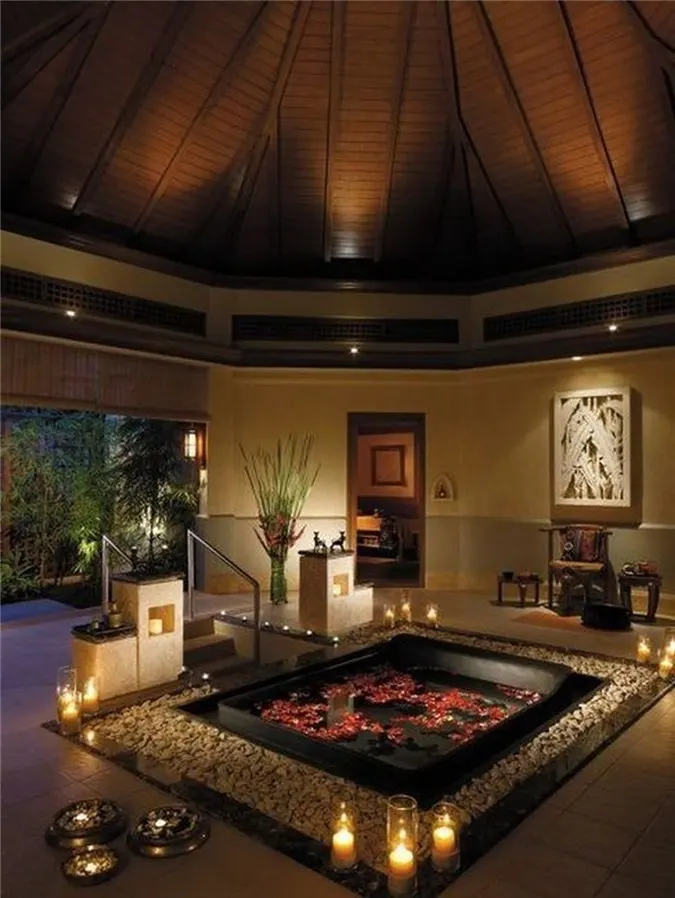 Bồn tắm chìm với đá cuội và nến xung quanh, với cánh hoa và cầu thang để tối đa hóa sự thoải mái