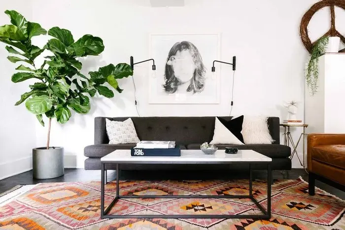 Đồ nội thất tối màu tạo thêm chiều sâu cho phòng khách nhỏ màu trắng. Ghế sofa màu xám và ghế phụ không làm không gian phòng nhỏ đi. Nếu có trần nhà cao, bạn có thể để cây trong nhà nhằm tạo sự tương phản với bức tường trắng. Tấm thảm dưới sàn có tông màu cam giúp căn phòng hài hòa hơn.