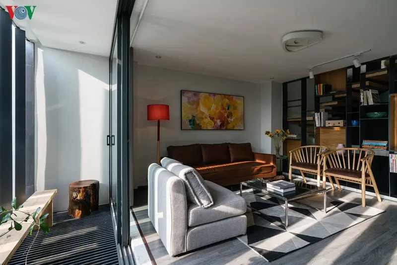 Phía trước phòng khách có một khoảng hiên. Sàn nhà và đồ nội thất có màu xám chủ đạo điểm xuyết với một số màu khác.