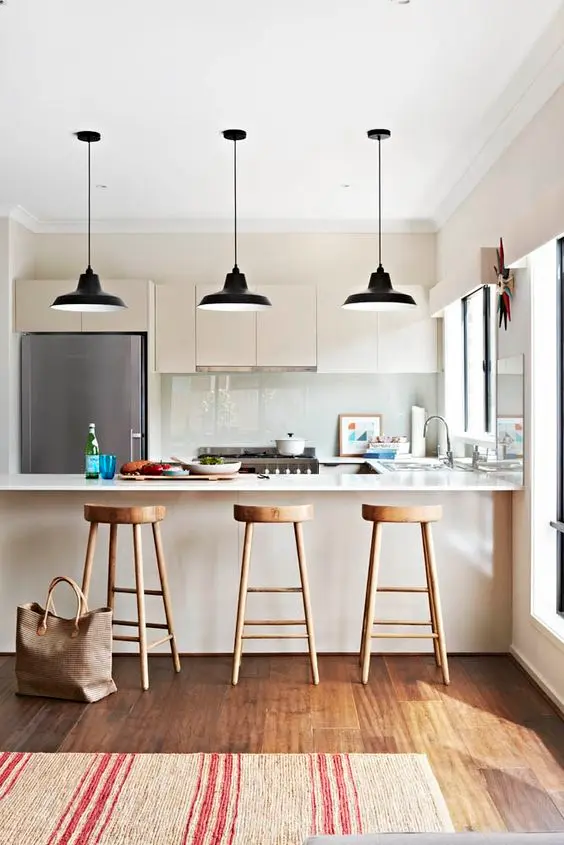 tủ bếp màu trắng ngà xinh xắn với tủ kiểu dáng đẹp, mặt bàn bằng đá trắng và máy hút mùi tích hợp cùng với đèn mặt dây chuyền màu đen