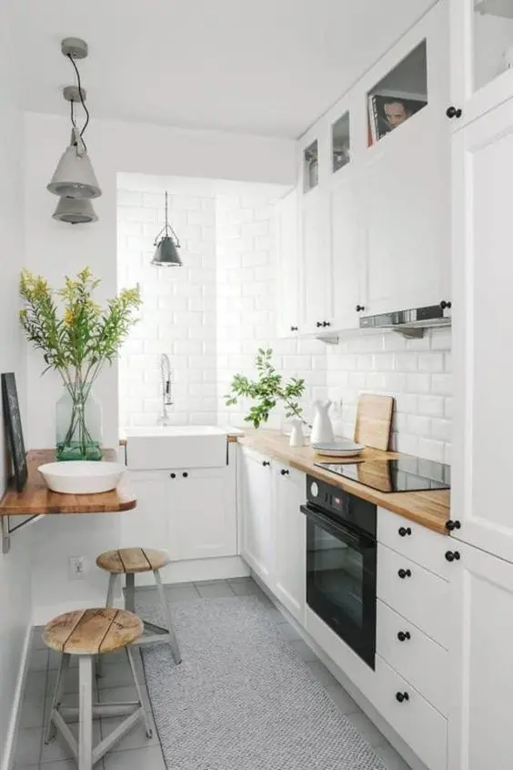 căn bếp nhỏ màu trắng ấm cúng với máy hút mùi kết hợp, mặt bếp bằng butcherblock và các thiết bị tích hợp cùng với khu vực ăn uống nhỏ
